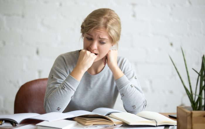 Portrait of a student girl sitting at the desk biting her fist
